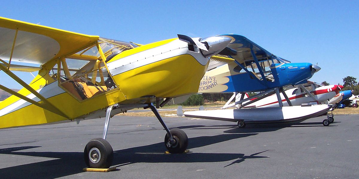 vintage planes on tarmac. yellow plane in foreground, blue and yellow seaplane in background.