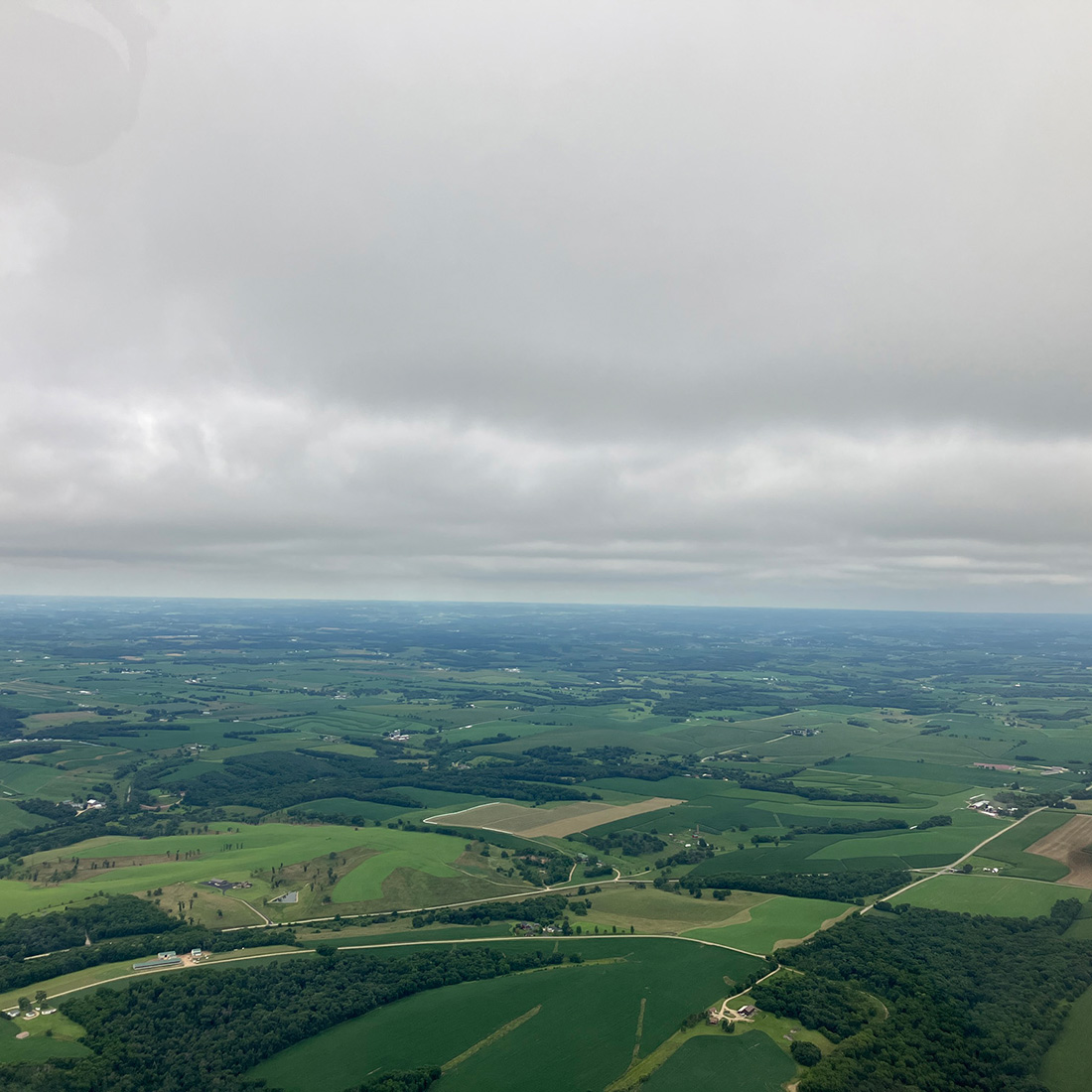 view of green farmland and gray skies from cessna